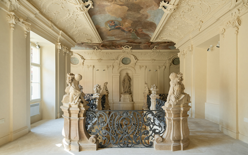 An elegant room featuring intricately carved statues, ornate stucco ceiling, and a detailed, ornamental iron gate.