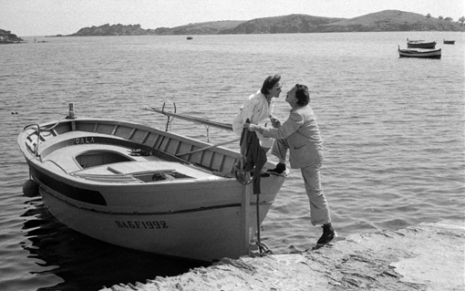 Two individuals interact by a docked boat named "GALA" with a scenic backdrop of hills and water.