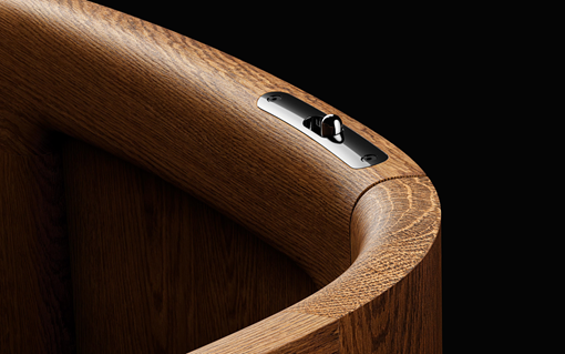 A close-up of a polished wooden surface with a metallic switch embedded in it against a black background.