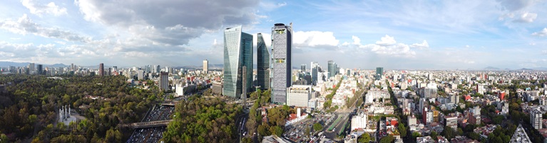 Aerial view of Mexico City with modern skyscrapers towering over busy streets and green areas.