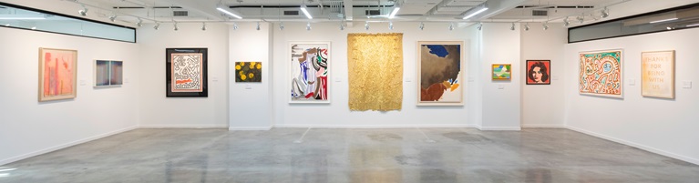 A modern art gallery displays colorful and diverse paintings on white walls with bright lighting.