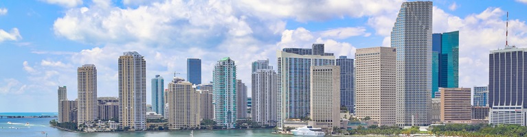A panoramic view of the modern Miami skyline featuring numerous high-rise buildings and a waterfront.