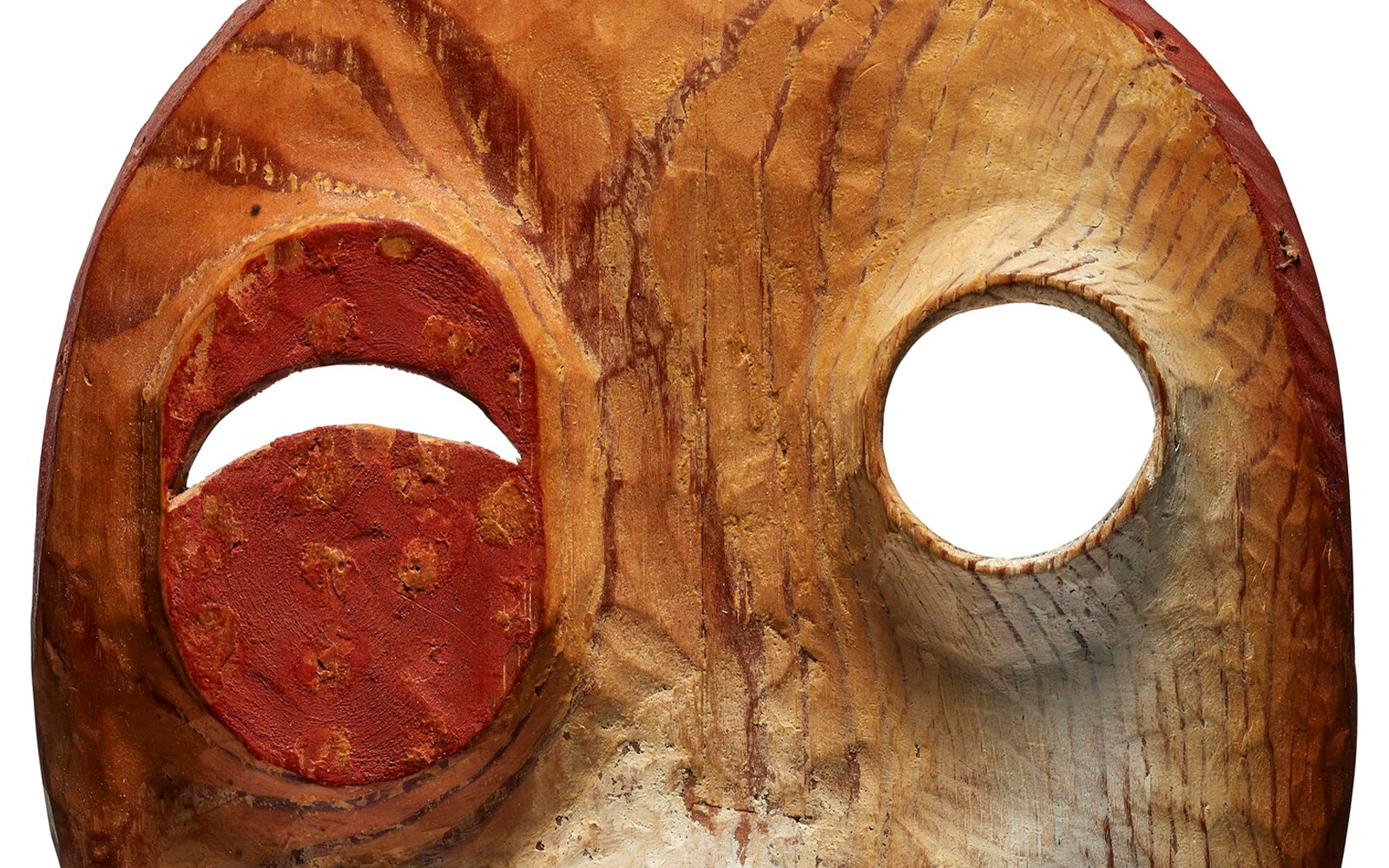 Close-up of a weathered wooden mask with prominent eye holes surrounded by red paint.