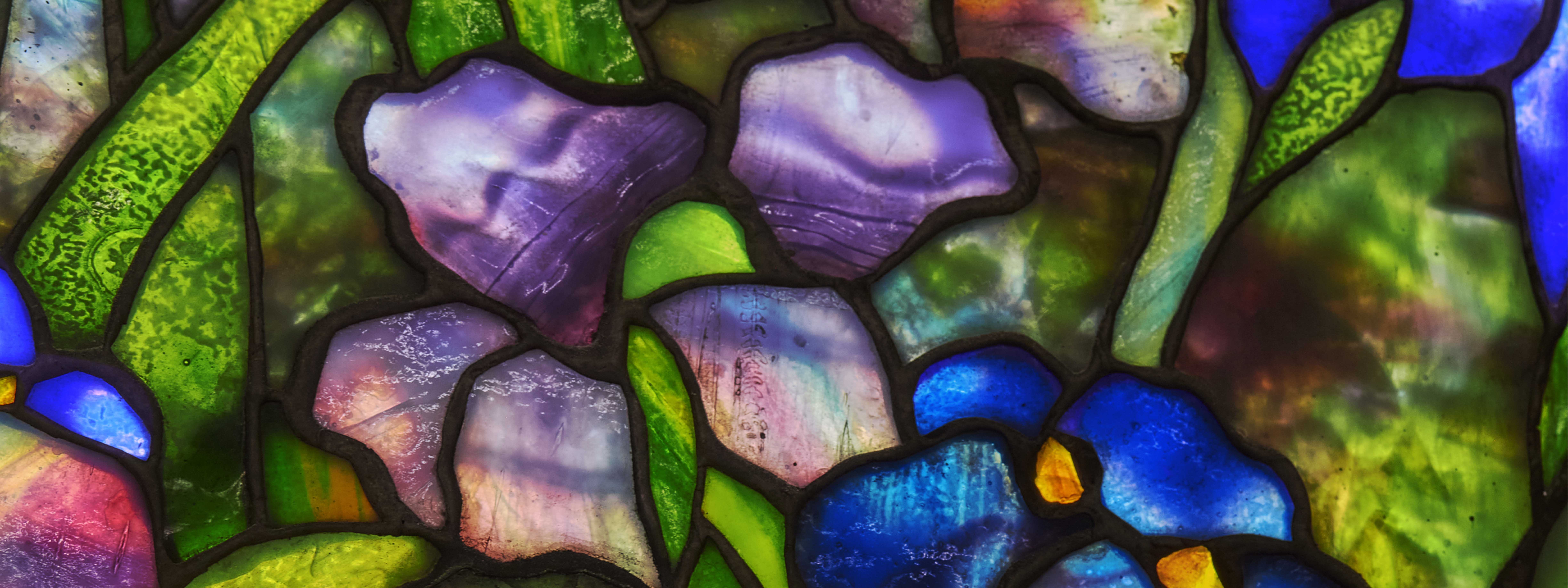 Colorful stained glass panel featuring abstract, floral-like patterns in blues, greens, and purples.