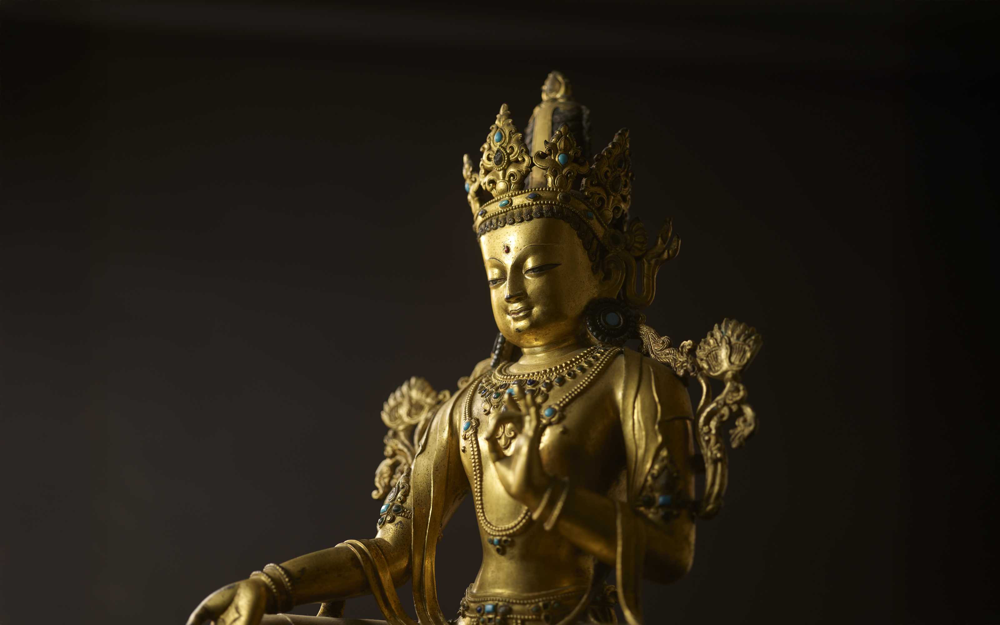 The image shows a golden statue adorned with intricate jewelry and a detailed crown, set against a dark background.