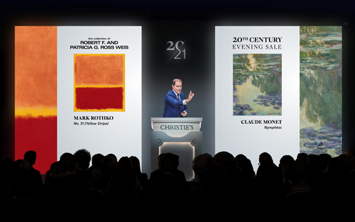 A crowd at an art auction watches a presentation featuring artwork by Mark Rothko and Claude Monet.