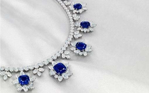 A diamond necklace with five large blue sapphires set in floral arrangements is displayed on a light satin background.