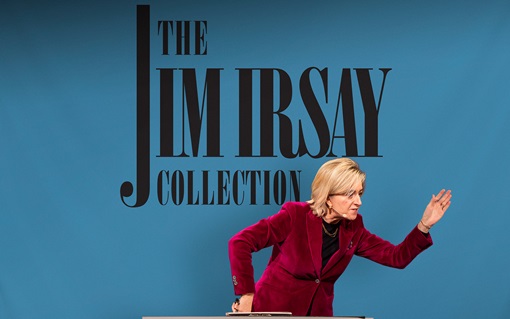 A person in a red blazer gestures in front of a sign reading "The Jim Irsay Collection."