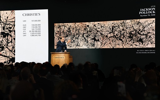 An auctioneer at Christie’s sells Jackson Pollock’s abstract painting to a large crowd.