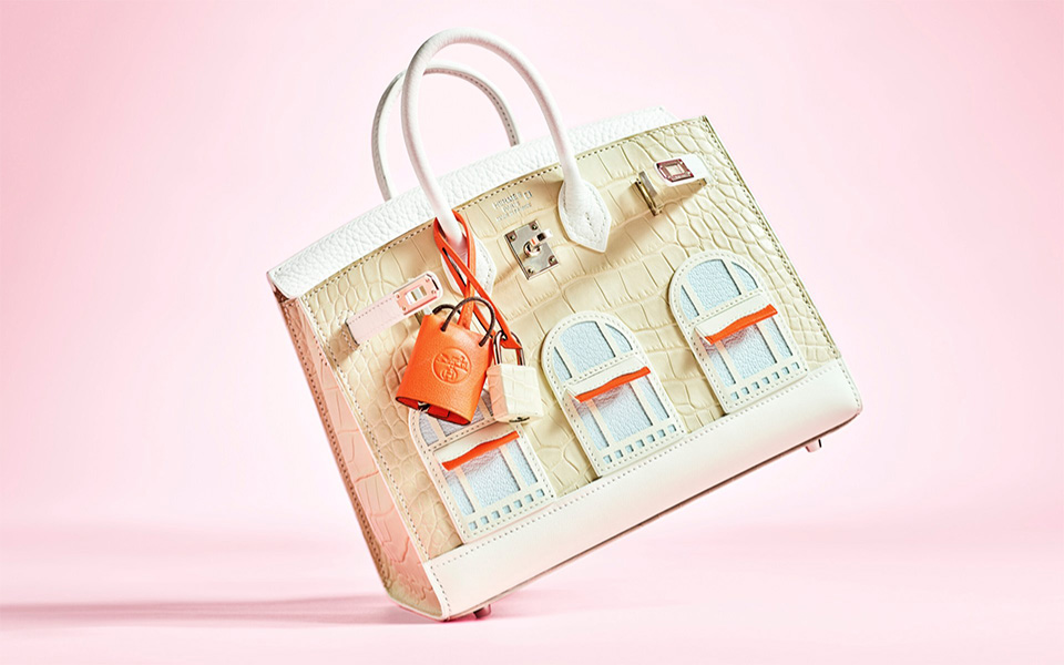A designer handbag with architectural window details and orange accents on a pink background.
