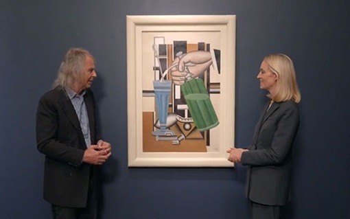 Two people stand on either side of a framed abstract painting on a dark blue wall.