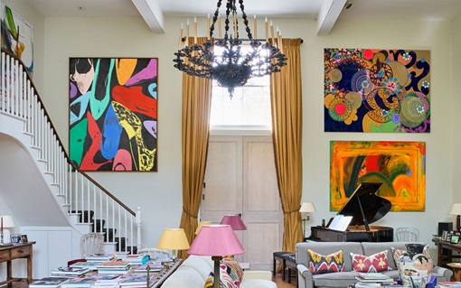 A brightly lit living room with colorful abstract art, a grand piano, and eclectic decor.