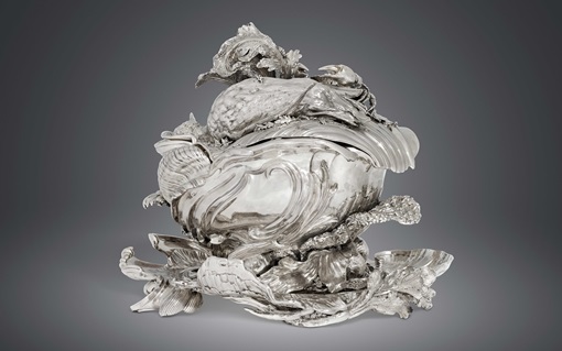 A decorative silver vessel featuring intricate designs of birds and foliage.