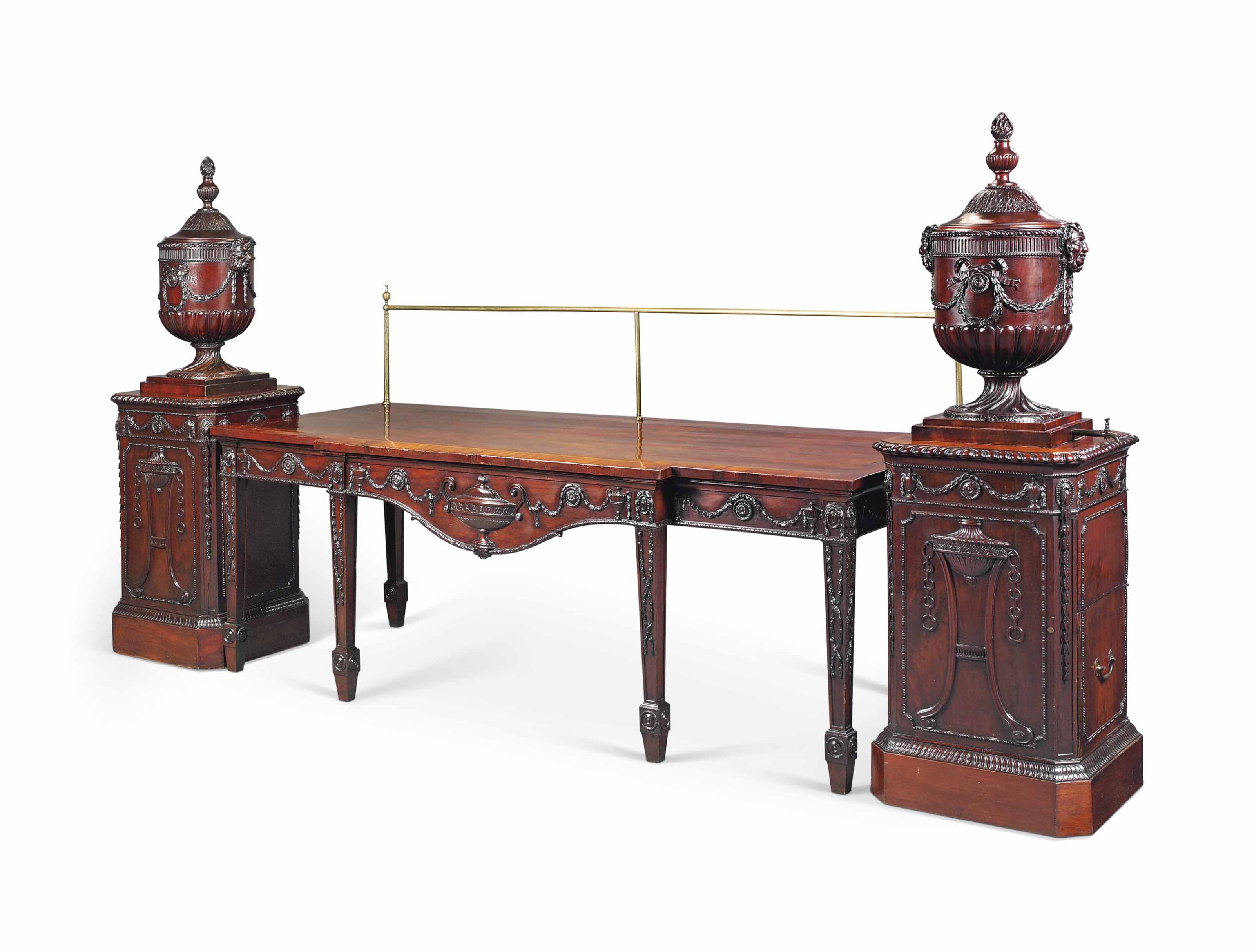 A George III mahogany serving-table and pair of urns and pedestals en suite, attributed to Mayhew and Ince, circa 1770-72. The serving-table: the brass rail with urn-finials, above a green-stained harewood-strung and crossbanded breakfront top and shaped apron centred by a large urn with guilloche-carved frieze and carved with further husk swaged urns and paterae, with rosette and ribbon borders, on six square tapering panelled legs headed by oval paterae and carved with further entwined husks, terminating in roundel-headed spade feet, inscribed 'butler 1892' (possibly the polisher), with two paper labels printed 'irwin untermyer collection' and numbered '97f'. 34½  in (88  cm) high, the table; 54  in (137  cm) high, overall; 96  in (243.5  cm) wide; 41  in (104  cm) deep. The urns and pedestals: each domed lid surmounted by a flaming gadrooned vase-shaped finial and carved with stiff leaf, on an urn carved with milled frieze, the body with ribbon-tied husk swags centred by paterae and flanked by satyr masks, the base gadrooned and the socle carved with spiral fluting, one urn with a removable silvered copper bucket, the other water urn lead-lined, above a pedestal carved to its front with a tripod perfume burner, the frieze with husk swaged urns and paterae flanked by oval paterae releasing further husk trails to the canted corners, terminating in leaf-carved banding, on a plain base, one with cupboard door to one side, enclosing a single plate rack, the other with lead-lined drawer above a cupboard door to one side, enclosing an open compartment, the water urn and pedestal with paper labels printed 'irwin untermyer collection' and numbered '99f/a', the tap and lower plinth base replaced. 73  in (185.5  cm) high; 23¼  in (59  cm) square. Sold for £137,000 on 6 July 2017 at Christie’s in London