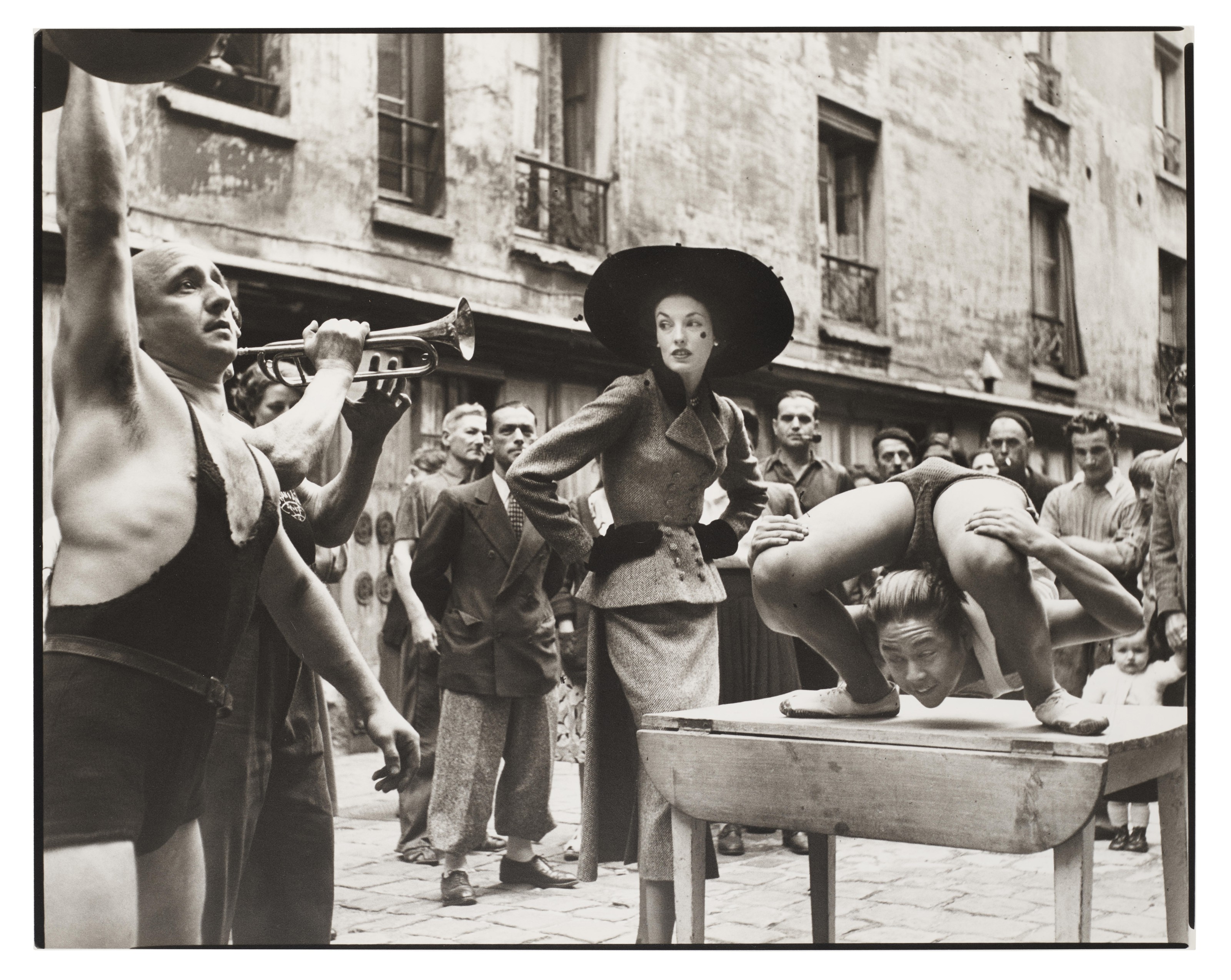 Richard Avedon (1923-2004), Elise Daniels with Street Performers, Suit By Balenciaga, Le Marais, Paris, 1948. Gelatin silver print, printed 1978. Sheet: 14&frac14; x 17⅞ in (36.2 x 45.3 cm). Estimate: $15,000-25,000. Offered in 
Fashion Photo, 2-11 December 2019, Online