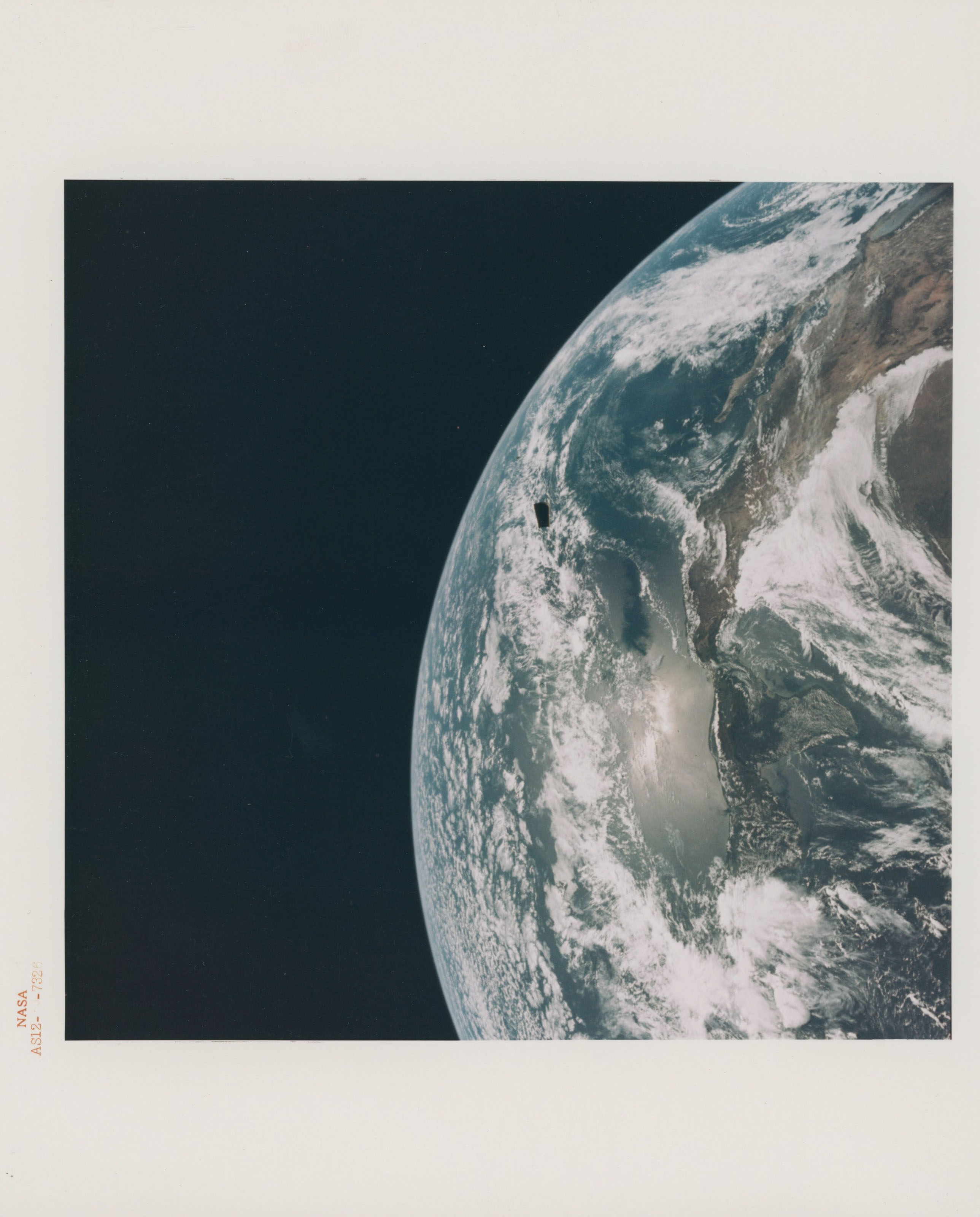 The Earth with the Spacecraft-LM Adapter drifting near the horizon; the ...