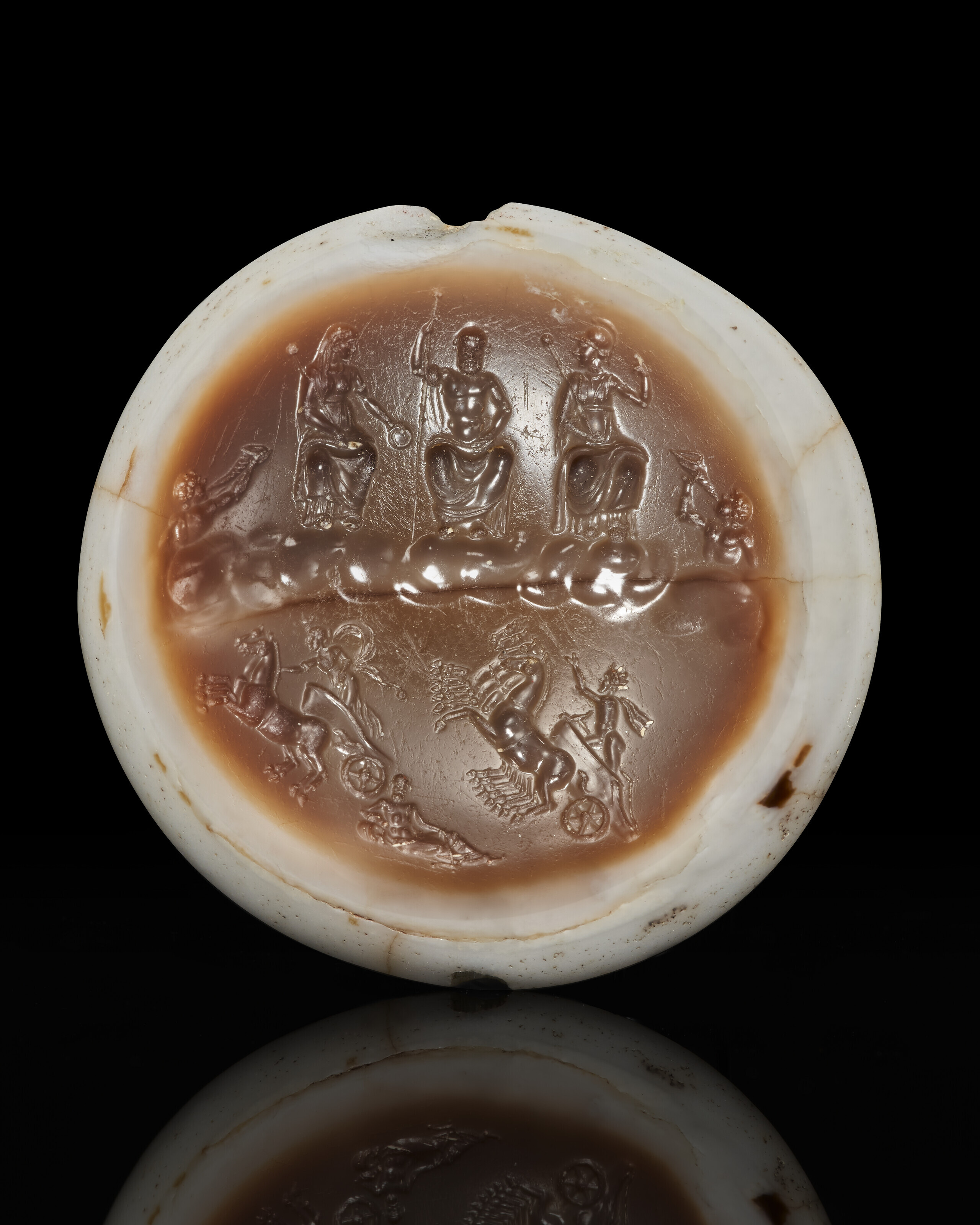 A Roman sardonyx ringstone with the capitoline triad, Imperial period, c. 1st century AD. 1⅛  in (2.8  cm) wide. Estimate: $15,000-20,000. Offered in Masterpieces in Miniature: Ancient Engraved Gems formerly in the G. Sangiorgi Collection Part III on 1-14 April 2022 at Christie’s Online