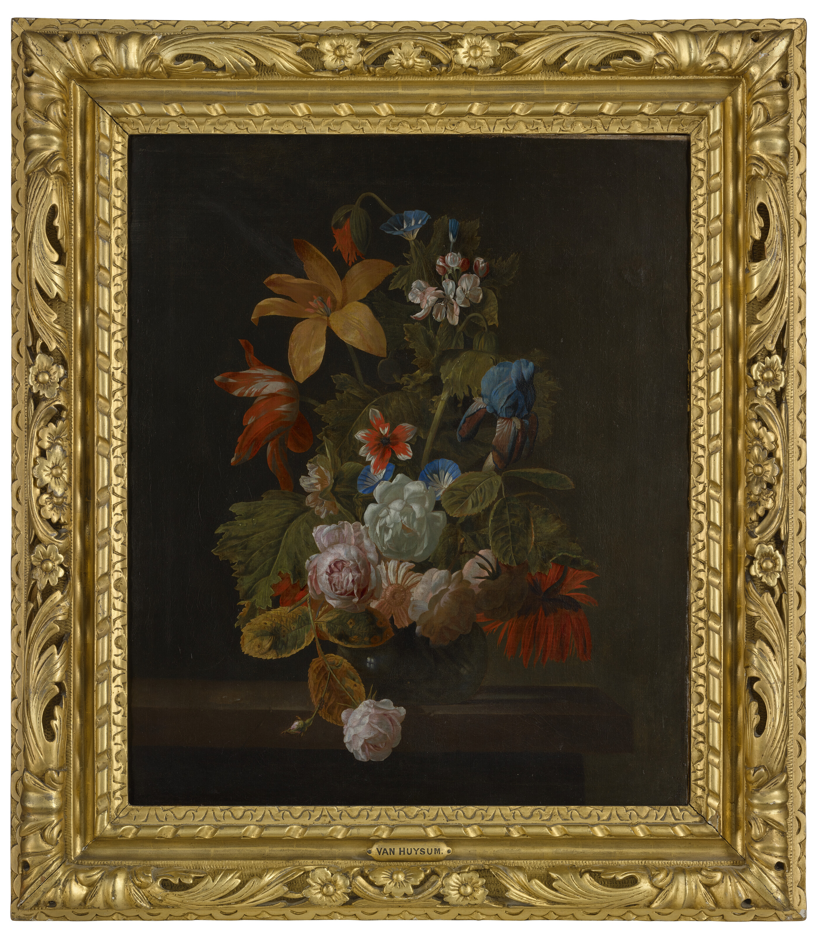 Catalog image of Tulips, roses, an iris and various flowers in a glass vase on a stone ledge