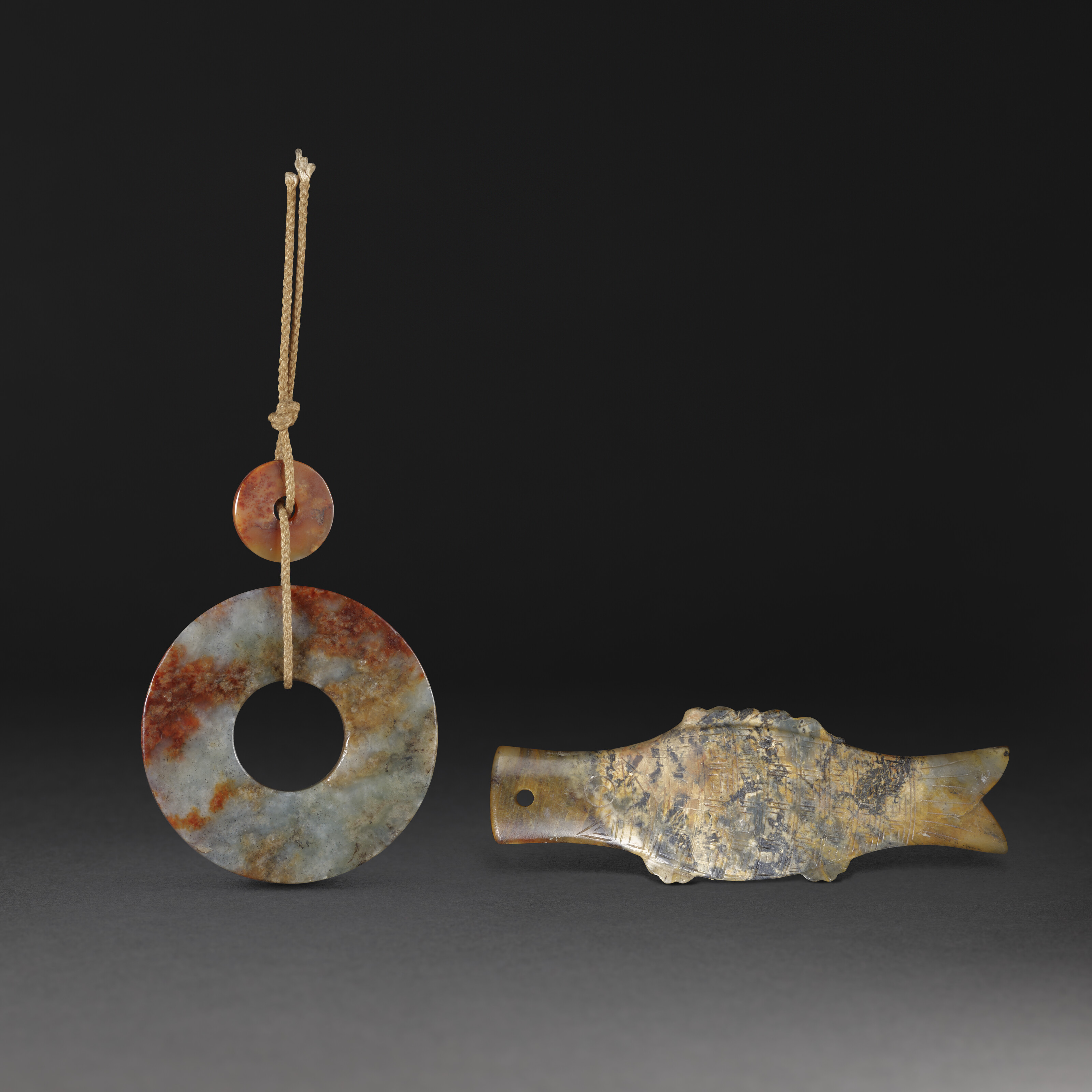 A MOTTLED GREEN AND BROWN JADE BI AND A JADE 'FISH' PENDANT, HAN