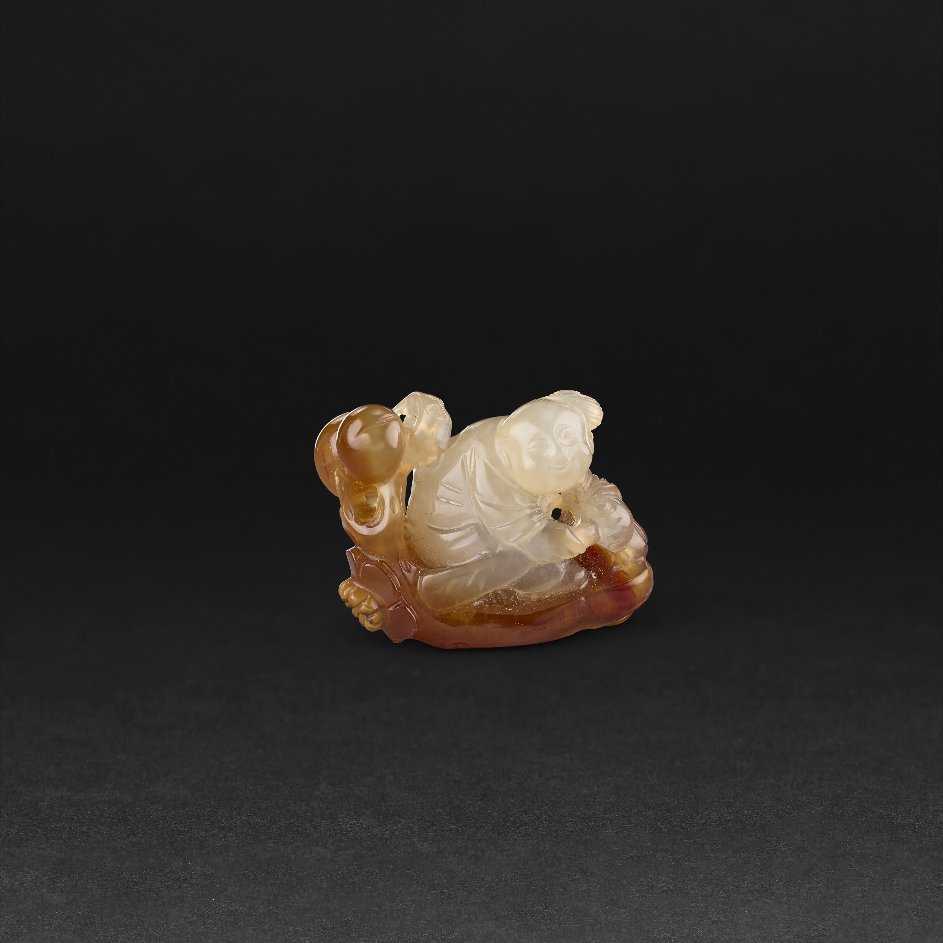 A GROUP OF TWO WHITE JADE 'RECUMBENT BOY' PENDANTS AND AN AGATE