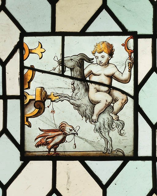 A RECTANGULAR STAINED GLASS PANEL DEPICTING A PUTTO SEATED ON A GOAT