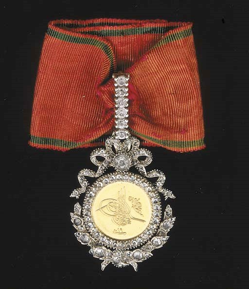 TURKEY, Order of Glory, circular paste-set Badge, 42 x 32mm., excluding suspension, the central medallion bearing an interesting variation of what is believed to be the Sultan's toughra of 1831-39, enclosed by a silver band, in turn enclosed by a silver riband above, and wreath below, the whole set with paste stones, with 20mm. long silver suspension fitted with six paste stones, signs of refurbishment commensurate with age, good very fine, with a length of old riband, in a contemporary oval red leather case