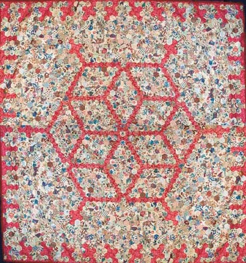 A patchwork coverlet, pieced with a diamond design from hexagons of bright polychrome chintz against a red ground--90 x 84in. (229 x 213.5cm.), circa 1860s with some earlier fabrics, backed in printed cotton, trimmed in later red braid