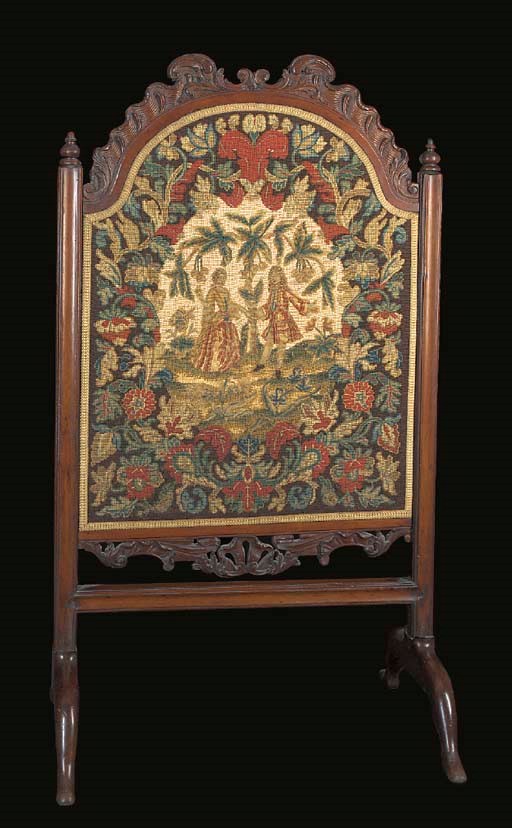 A needlework firescreen, worked in coloured wools in gros point, with petit point details, a central couple beneath a cherry tree within an elaborate floral border--51½ x 28¾in. (131 x 73cm.), including carved wooden frame, the needlework early 18th century