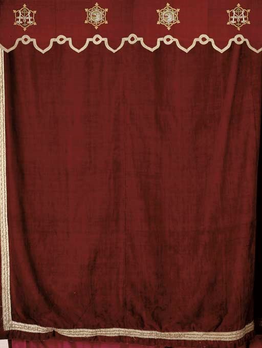 A PAIR OF RED WOOL PLUSH CURTAINS AND MATCHING PELMET APPLIED WITH THE MYDDELTON AROMORIAL VELVET MEDALLIONS