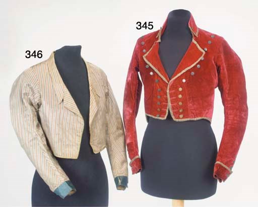 A lady's military style double-breasted spencer of crimson velvet, possibly a riding jacket, with high stand-fall collar and two rows of flat metal buttons running from shoulder to waist, the long shaped sleeves with small cuff and buttoned detailing, with pleated lower back, trimmed with metallic braid, faced with red and blue silk and lined with cotton, circa 1800, slight wear