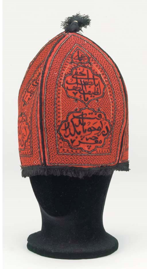 An embroidered conical hat of red wool facecloth, composed of four sections, each worked in black silks with three cartouches enclosing embroidered calligraphy, the surround with geometric patterning outlined in metal and silk thread, trimmed with black silk fringes and lined with printed cotton--9in. (23cm.) high, Persian, 19th century, dated 1847, metal thread mostly worn
