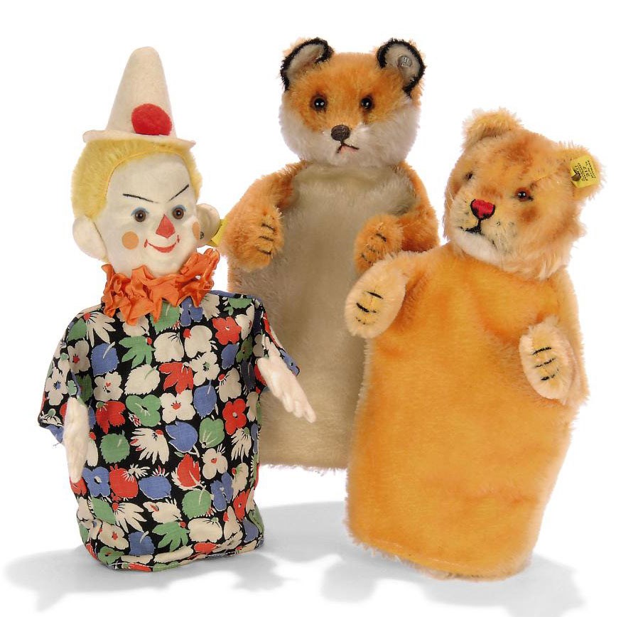 THREE STEIFF PUNCH-GLOVE PUPPETS, (317 and 217), a Punch-Fox, reddish-brown and white mohair, brown and black glass eyes, black mohair ear edges, black stitching and FF button, circa 1918; a Punch-Lion, yellow-brown mohair, brown and black glass eyes, red and black stitching, whiskers and FF button with yellow cloth tag, 1930s; and a Punch-Clown, (217), pressed felt face, ears and hat, brown and black glass eyes, yellow mohair hair, printed cotton body, orange ruff, red pom-pom and FF button with yellow cloth tag, late 1930s --9in. (23cm.) high	 (3)