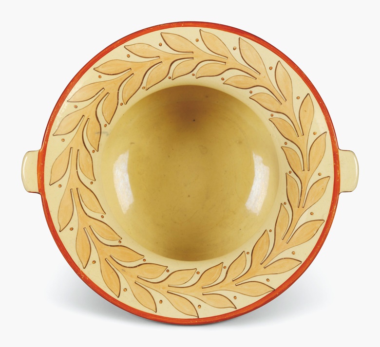 A Staffordshire pottery buff-ground two-handled basin from Napoleons ‘chamber service’, circa 1815. Possibly by Enoch Wood and retailed by George Bullock. The everted rim decorated with a band of orange berried laurel, the handles and rims edged in iron-red, the shoulder and foot with orange bands. 13 in (33 cm) wide. Estimate £1,000-1,500. This lot is offered in Interiors on 14