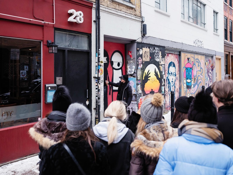 Stik touches up A Couple Hold Hands in the Street  on Brick Lane in London, to the delight of an onlooking crowd of Danish tourists