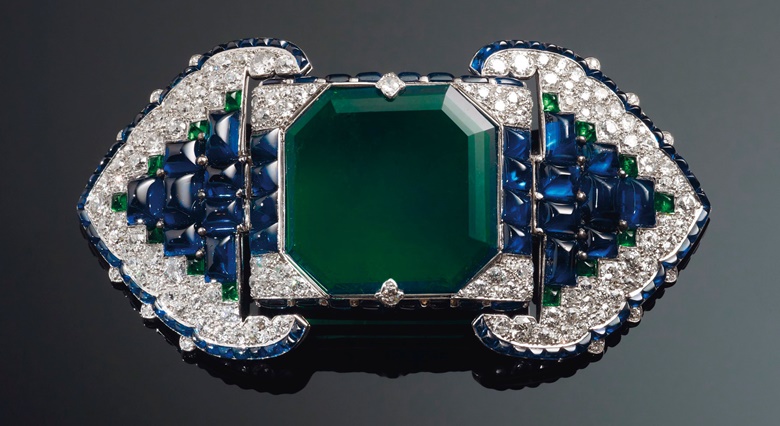 An Art Deco emerald, sapphire and diamond belt buckle-brooch, Cartier. Octagonal step-cut emerald of 38.71 carats, buff-top calibré-cut sapphires and emeralds, old and single-cut diamonds, platinum and 18k white gold (French marks), 3½ in, 1922. Unsigned, partial maker’s mark (Atelier Renault), no. 0346, red Cartier case