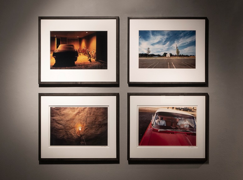 Installation view of four works by William Eggleston (b. 1939). Clockwise from top left Untitled (Car and Bicycles in Garage, Memphis, TN), 1970; Untitled (White Building Across Parking Lot) from ‘Los Alamos’, 1965-74; Untitled, (Couple in Red Car at Drive-In Restaurant, Memphis, TN), 1965-68; Untitled (Light Bulb on Plywood Ceiling, Greenwood, Mississippi), 1973. Photo © CAMERA