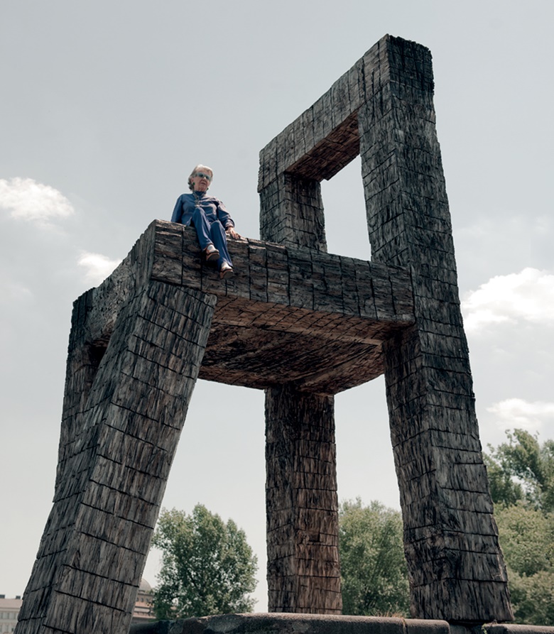 Meda Mládek sitting on a replica of Chair, 1980, by Magdalena Jetelová. The original work, installed on a breakwater in the Vltava River adjacent to the museum, was swept away by floods in 2002. The chair seen here, made from flood-damaged trees, was created by artist Kurt Gebauer’s students at Prague’s Academy of Arts, Architecture and Design. Photo Pavel Brunclík