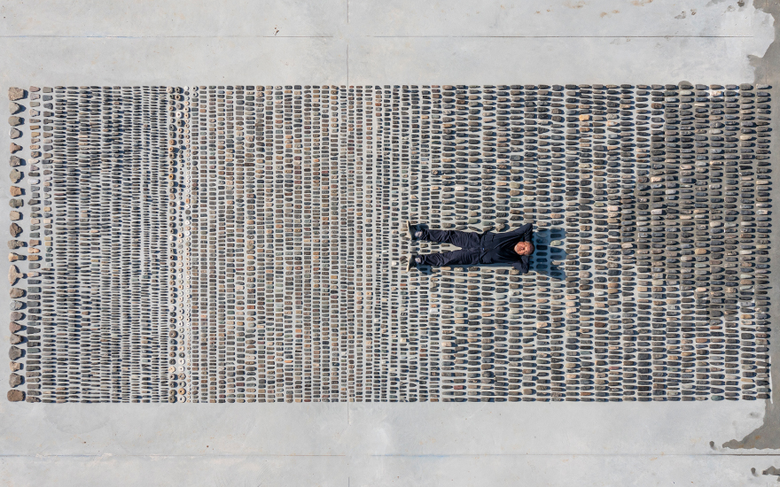 Ai Weiwei lying on a rectangle of stone artefacts. © Image courtesy Ai Weiwei Studio
